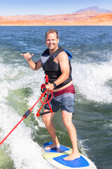 Adult male smiling and enjoying a day on the lake while he attempts to wake surf behind a motor boat. Smiling handsome mature man active lifestyle