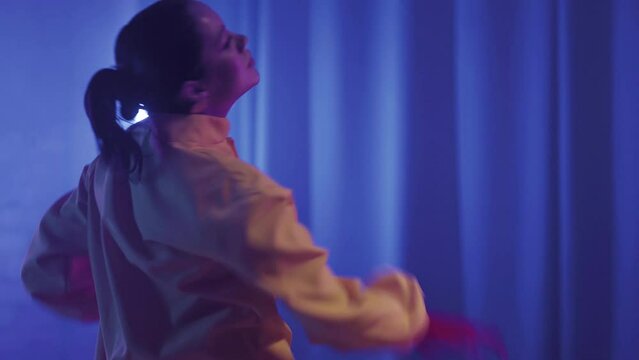 A beautiful girl is dancing indoors under blue lighting in a yellow suit. Dances