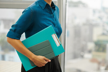 Cropped image of businesswoman carrying documants folder and digital tablet to meeting