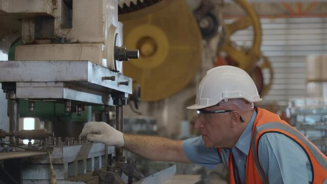 Engineer or operator wearing a safety suit working bending metal sheet by sheet press bending machine in workshop, Worker in factory at metal folding machine putting work piece at factory industry