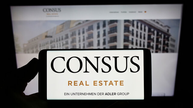 Stuttgart, Germany - 05-20-2022: Person holding smartphone with logo of German company Consus Real Estate AG on screen in front of website. Focus on phone display.
