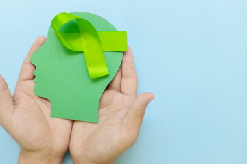 Hand holding human head profile with lime green awareness ribbon on brain. Lyme disease, psychosis, childhood mental illness, lymphoma and postpartum depression care concept.