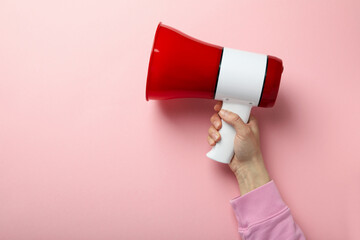 Female hand with megaphone on pink background
