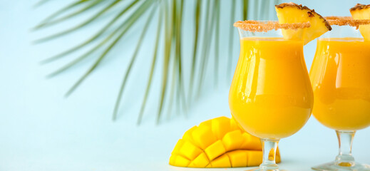 Glasses of tasty mango smoothie on light blue background