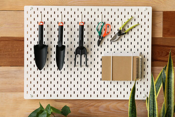 Pegboard with gardening tools and houseplants near wooden wall