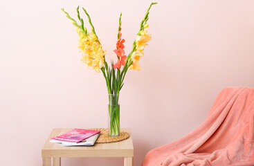 Vase beautiful gladiolus flowers and magazines on table in room