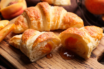 Wooden board of delicious croissants with peach jam on table, closeup