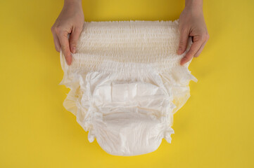 A woman holds an adult diaper on a yellow background. Incontinence problems. - obrazy, fototapety, plakaty