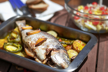 Delicious baked whole fish with herbs and lemon in a metal baking tray. selective focus. close up.