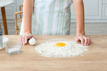 Young woman making dough on table in kitchen, closeup