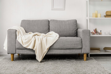Grey sofa with plaid and shelving unit near light wall - obrazy, fototapety, plakaty