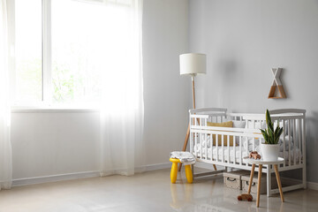 Interior of light nursery with baby crib, lamp and table