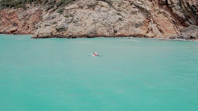 Aerial circular view of family rowing on stand up paddle boards. Mom and dad oaring on paddleboards with their sons down azure sea
