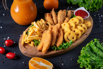 fried french fries with fried chicken sticks with tomato sauce and orange juice . on a black wooden background