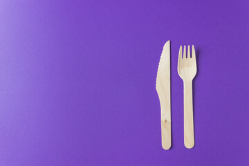 Disposable tableware from natural materials - wooden fork and knife isolated on a violet background.