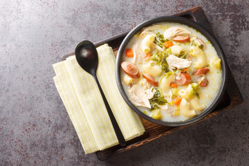 Filipino chicken soup with elbow pasta, vegetables, sausages close-up in a bowl on a wooden tray....