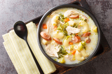 Asian chicken soup with elbow pasta, vegetables, sausages close-up in a bowl on a wooden tray....