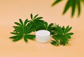 A white cosmetic jar on a beige background among green lupine leaves.