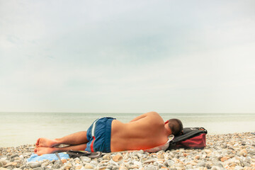 homme allongé de dos sur une plage de galets face à la mer © jef 77