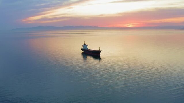 Bulk carrier ship at anchor in orange sunset, aerial view. Bright sunny path on water, red orange sky. Natural landscape. Shipping business sea shipping. Delivery logistics. Panorama from a drone