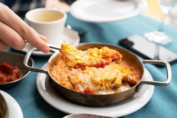 Turkish traditional tasty breakfast.Female hand holding fork with omelet.View from top, close-up shot.Delicious food of eggs concept