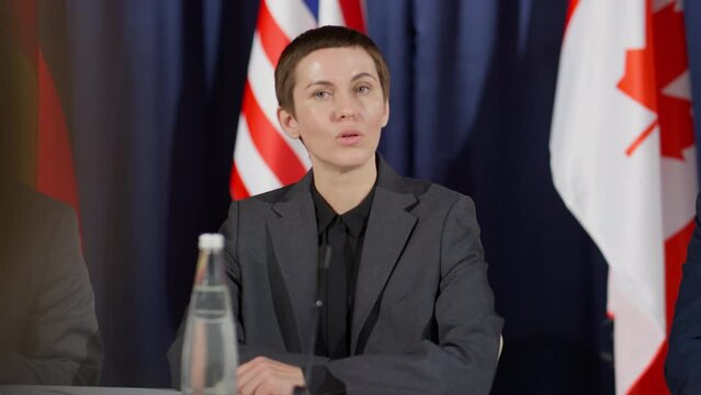 Young Caucasian female politician talking in mic while answering questions of journalists during international press conference