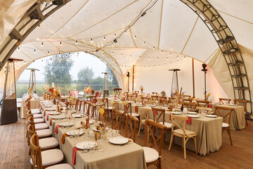 Served tables in tent prepared for wedding day on rainy day