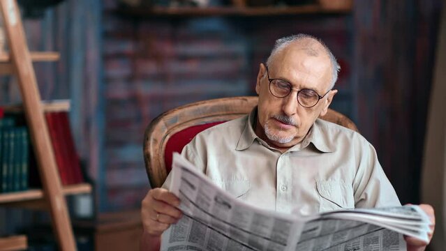 Gray haired aged mature man in eyeglasses reading daily press printing newspaper vintage armchair