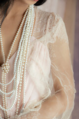 A woman's wearing a pink vintage dress with a lace shawl, and pearls against a soft fabric background