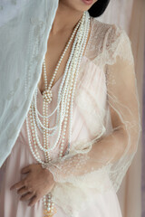 A woman's wearing a pink vintage dress with a lace shawl, and pearls against a soft fabric...