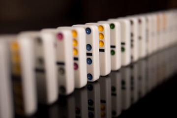 White domino bones stand on a black mirror surface. Domino effect. Domino effect and chain reaction concept. The background is blurry.