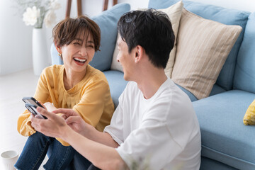 部屋でくつろぎながら携帯を見る仲良し若い日本人カップル・夫婦