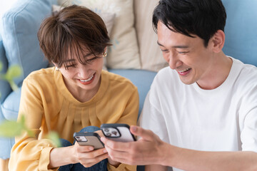 部屋でくつろぎながら携帯を見る仲良し若い日本人カップル・夫婦