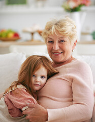 portrait of happy grandma with cute little redhead baby girl, sitting on sofa at home