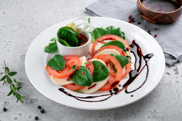 Caprese salad with tomatoes, mozzarella cheese, basil and balsamic sauce on a white plate on the kitchen table.