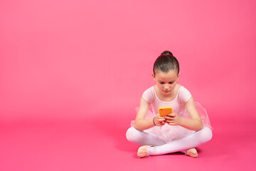 Little ballet dancer girl concentrated on phone isolated on vivid pink background.