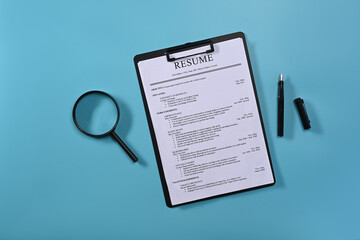 Flat lay magnifying glass and resumes applicants on blue background. Job search concept