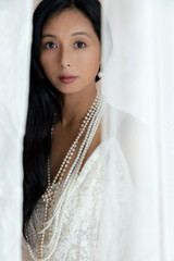 Beautiful Asian woman with long hair wearing a white lace dress and pearl jewellery surrounded by...