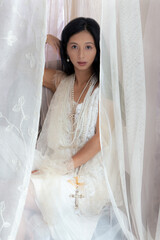 Beautiful Asian woman with long hair wearing a white lace dress and pearl jewellery surrounded by...