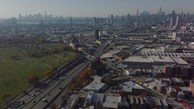 Aerial panoramic shot of large city. Busy multilane expressway leading along cemetery. Downtown skyscrapers in distance. Queens, New York City, USA
