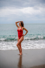 A beautiful and sexy brunette in a red swimsuit on a pebble beach, Running along the shore in the foam of the waves