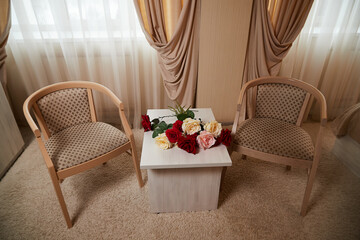 A living room with a light carpet, two armchairs, a small table and a window with darkened curtains. Location for a photo shoot