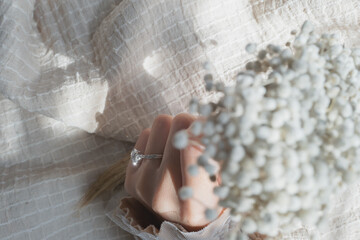 Close up of diamond ring on woman’s finger while holding white flowers with sunlight and shadow...