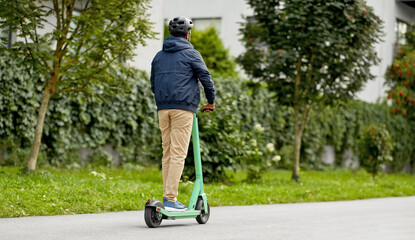 transport, safety and people and concept - young man in helmet riding electric scooter on city...