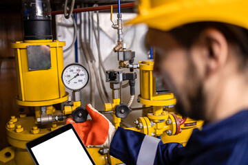 Oil and gas refinery worker measuring pressure of gas pipes and checking tablet computer.