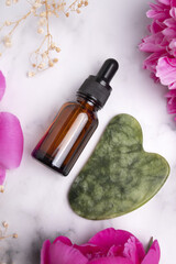 Glass bottle with oil, jade Gua sha stone for face massage on marble background with peony flowers