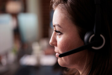 Female receptionist wearing headphones to work at call center helpdesk, giving telemarketing assistance. Woman working at customer service support to help clients, telephony network. Close up.