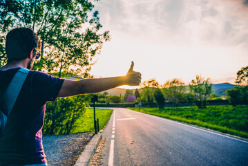 Man on the side of a road with thumbs up hitchhiking