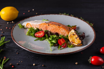 trout baked with lemon in a sauce with herbs and tomatoes. on a black wooden background