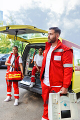 Naklejka premium Paramedic nurse and emergency doctor at ambulance with kit. a paramedic, standing at the rear of an ambulance, by the open doors.